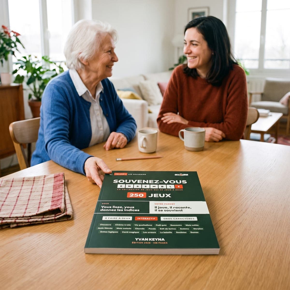 En äldre mamma och hennes dotter skrattar tillsammans vid bordet, boken ”Låt oss minnas tillsammans” framför dem